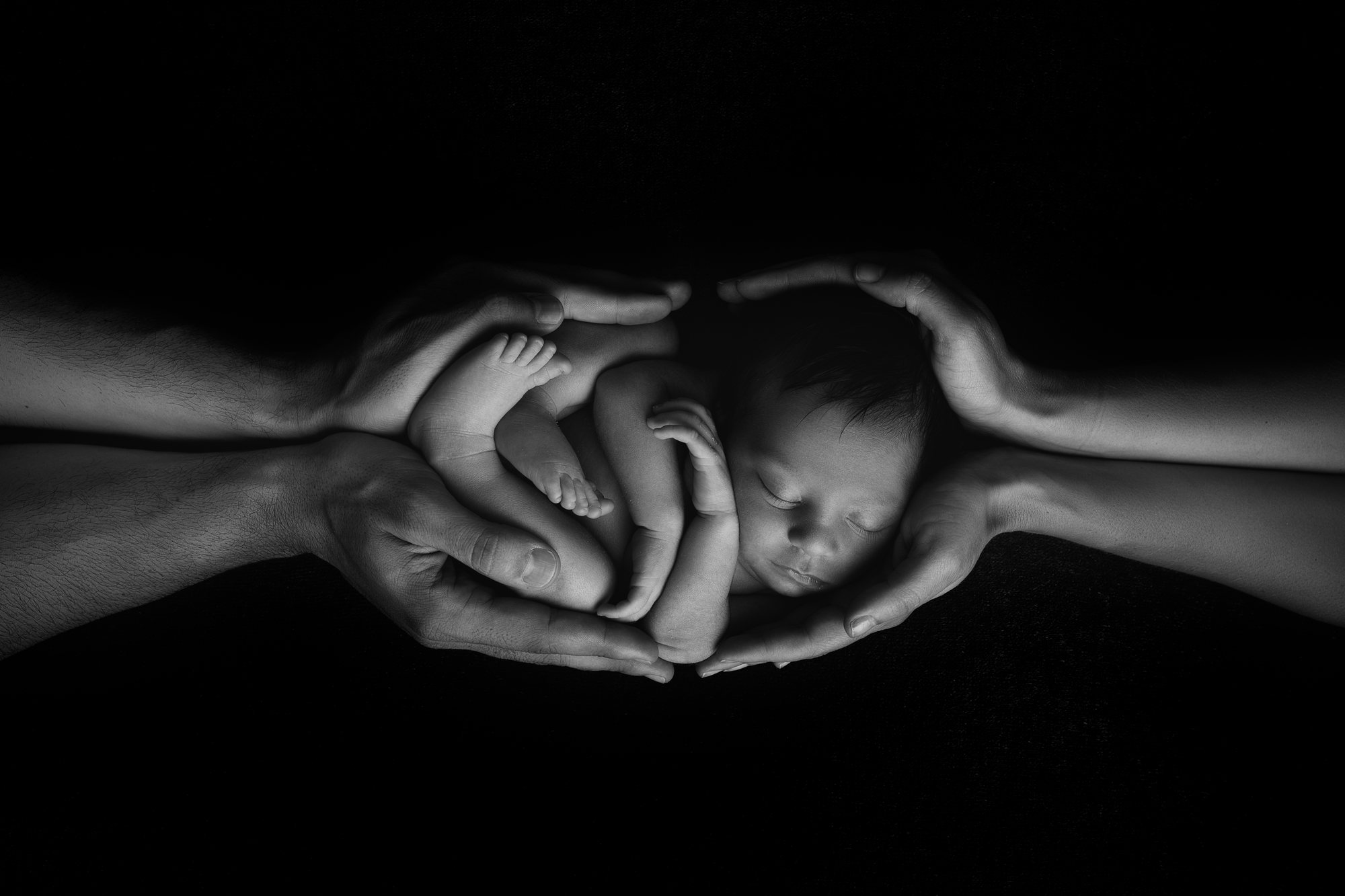 Mãos de dois adultos em concha à volta de um recém-nascido